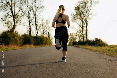 Fototapeta Naklejka Na Ścianę i Meble -  Young sporty girl running on a  road at sunset.   Lifestyle sports motivation. 