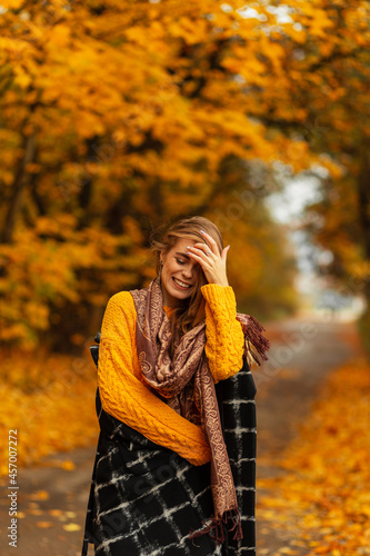 Emotional female portrait of a beautiful girl with a cute smile in a vintage yellow knitted sweater  black coat and scarf in nature with bright colored autumn foliage