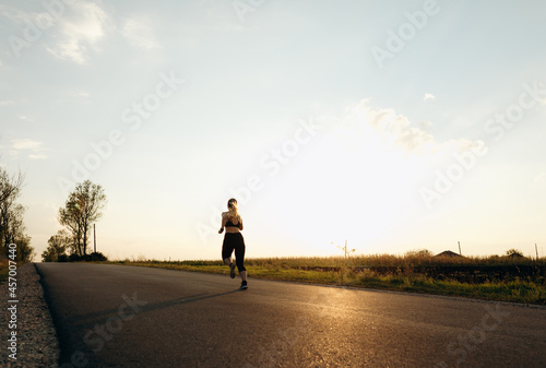 Young sporty girl running on a  road at sunset.   Lifestyle sports motivation. 