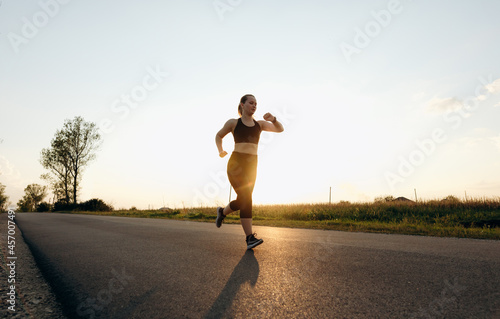 Young sporty girl running on a road at sunset. Lifestyle sports motivation. 