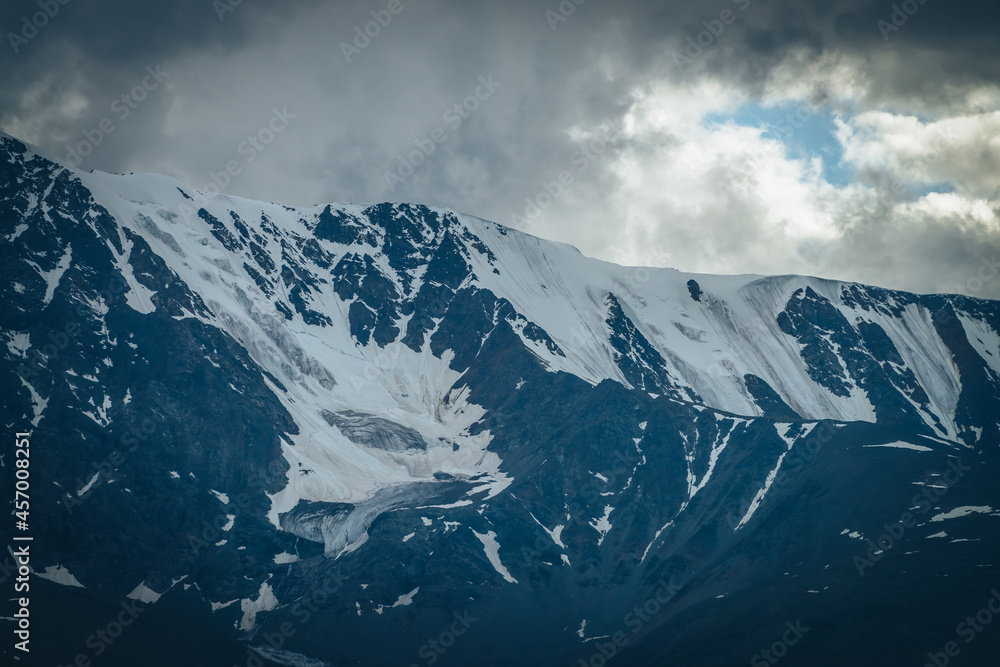 Dramatic mountains landscape with big snowy mountain ridge under cloudy sky. Dark atmospheric highland scenery with high mountain range in overcast weather. Awesome big mountain wall under gray clouds