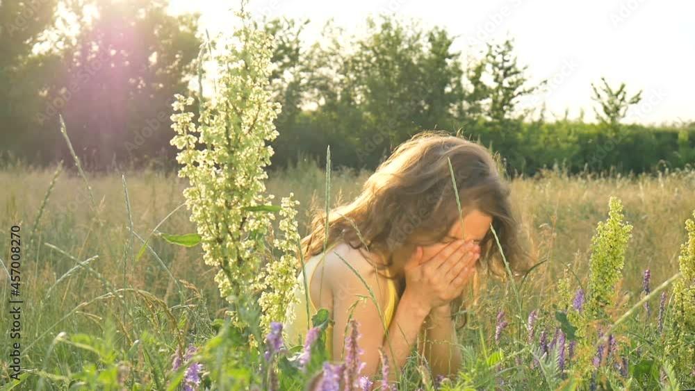 Pretty young girl is sitting in the middle of the field with flowers during summer time and sneezing, hypersensitivity, asthma, or allergy concept Pretty young girl is sitting in the middle of the field with flowers during summer time and sneezing, hypersensitivity, asthma, or allergy concept