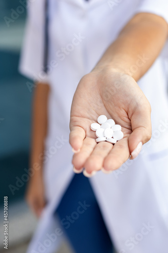Healthcare, medicine and people concept - Oriental female hands of a pharmacist in a medical gown holding a handful of white pills in the palm outside in good weather