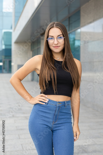 Lifestyle, femininity, body and people concept - A pretty, smiling, curvy girl in glasses, black tank top, and blue jeans standing on the street with one hand around her waist