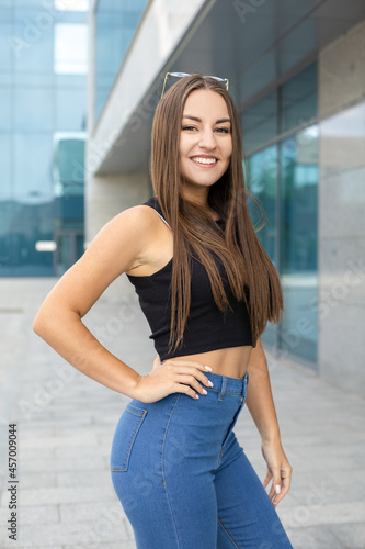 Lifestyle  body and people concept - A beautiful smiling sporty girl with straight dark hair and glasses on head wearing a black tank top and blue jeans standing outdoor with one arm around her waist
