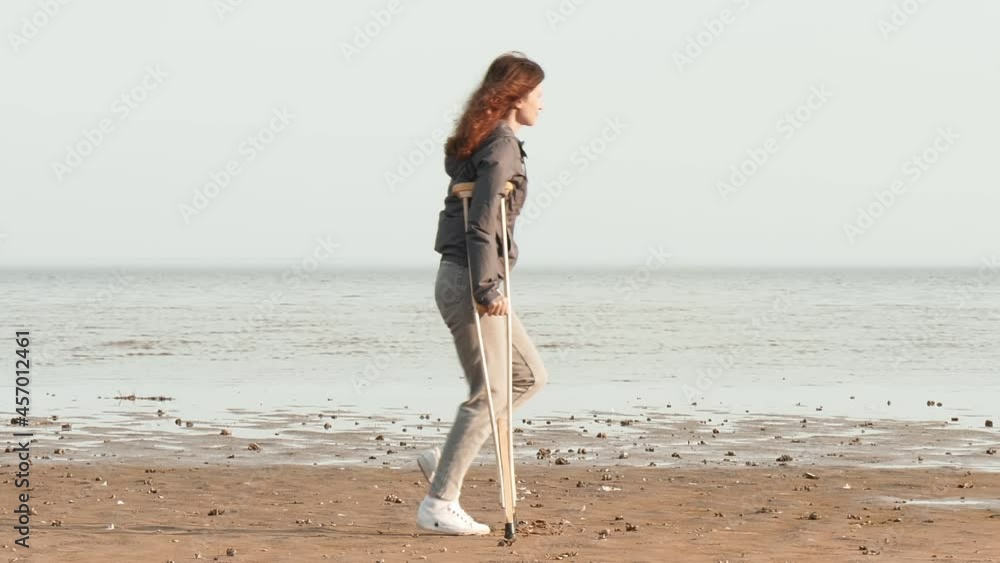 A woman on crutches walks along the beach, throws crutches and tries to