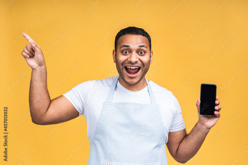 Black male african american indian cook or chef touching mobile phone display and pointing with index finger at blank screen, isolated over yellow background, copy space, cutout. Pointing finger. Black male african american indian cook or chef touching mobile phone display and pointing with index finger at blank screen, isolated over yellow background, copy space, cutout. Pointing finger.