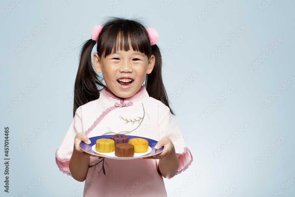 young girl holding traditional  Chinese moon cake against plain blue background