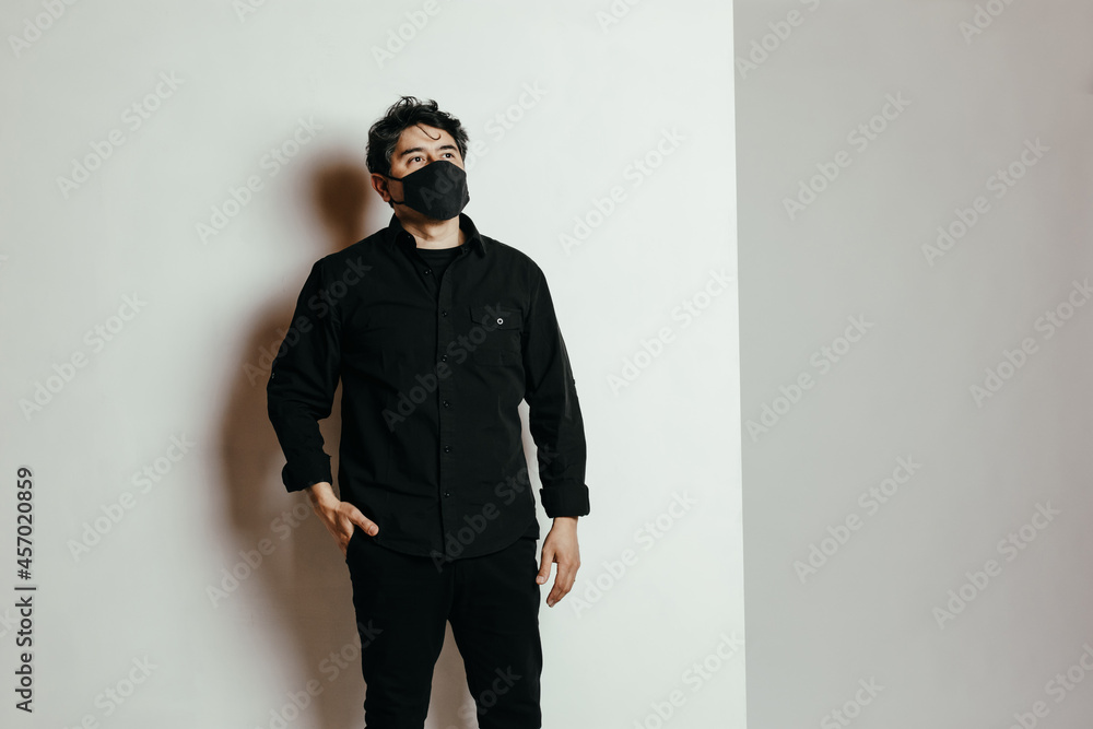 Hombre con camisa negra en fondo blanco con barbijo contra el Covid-19 mirando hacia un lateral Hombre con camisa negra en fondo blanco con barbijo contra el Covid-19 mirando hacia un lateral
