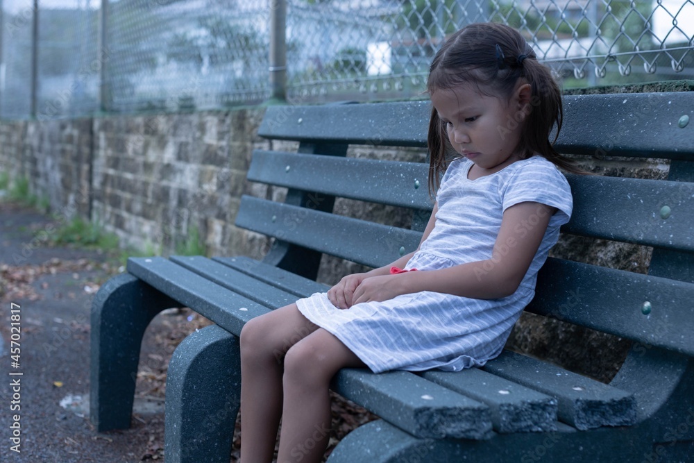 A sad little girl sitting alone outside on a bench depressed. A sad little girl sitting alone outside on a bench depressed.