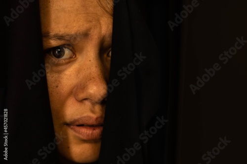 Frightened woman hiding behind a black curtain afraid and scared.