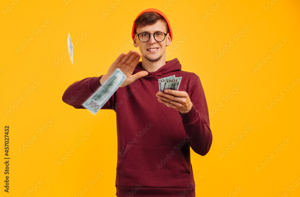 handsome guy wearing orange hat with glasses and red sweatshirt, throws one dollar bill, concept: successful young man handsome guy wearing orange hat with glasses and red sweatshirt, throws one dollar bill, concept: successful young man