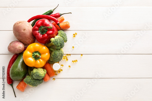 Fresh vegetables and pills on white wooden background