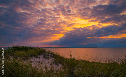 Seascape with red sunset behind dark bluish-purple clouds over sand dunes