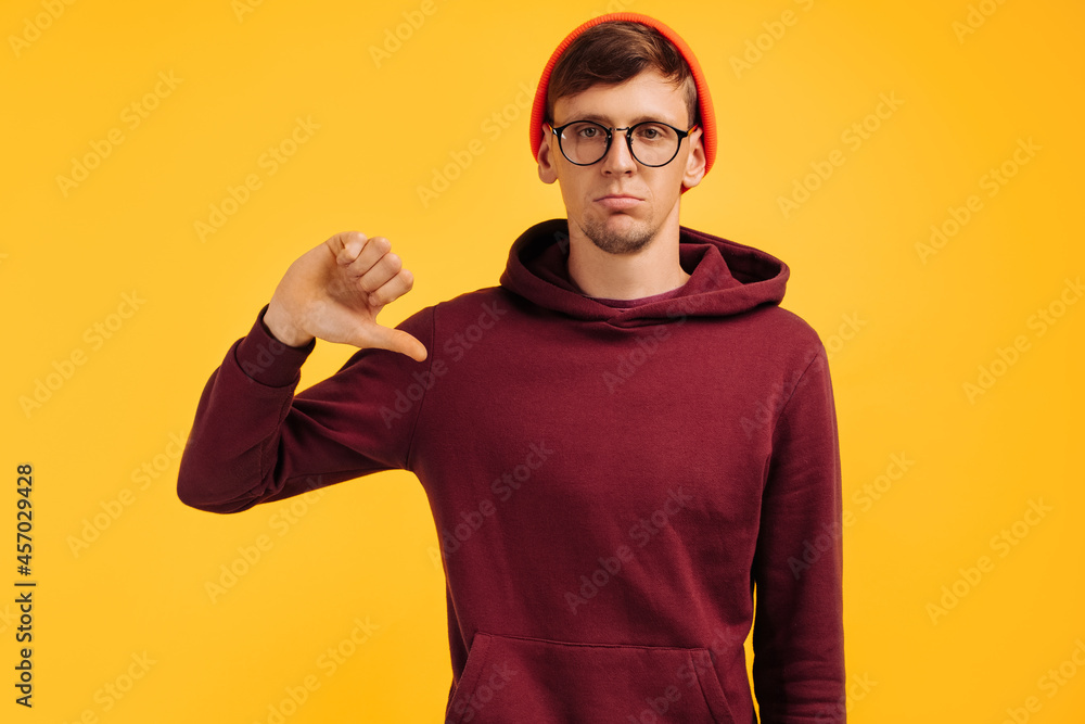man showing a thumb down dislike gesture, in an orange hat and a red sweater man showing a thumb down dislike gesture, in an orange hat and a red sweater