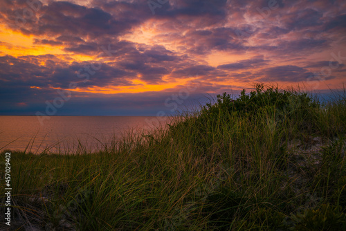 Blazing sunset with dramatic cloudscape over the grassy sand dunes in the shore on Cape Cod