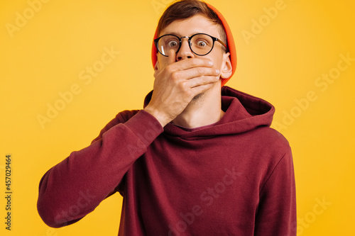 man covered his mouth with his hand, a frightened man, in an orange hat and red sweatshirt, and glasses