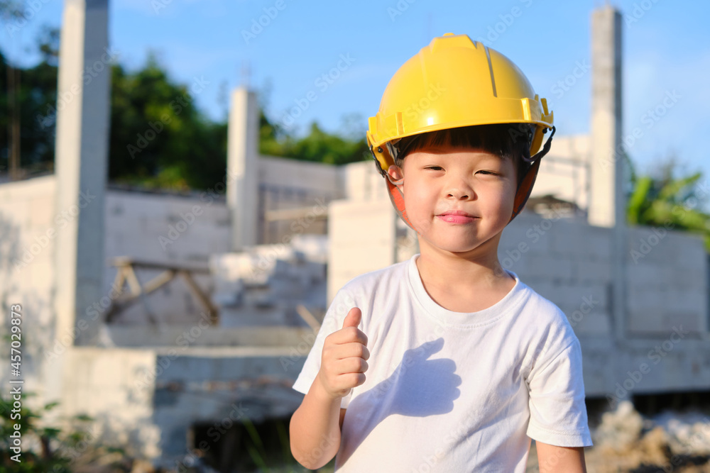 Cute Asian smiling happy kindergarten boy kid wearing yellow construction helmet or safety hard hat, Little engineer standing in front of construction site, Home building Project Cute Asian smiling happy kindergarten boy kid wearing yellow construction helmet or safety hard hat, Little engineer standing in front of construction site, Home building Project