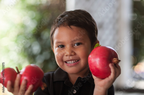 Smiling child holding up in his little hands some freshly cut pomegranates that are grown organically.