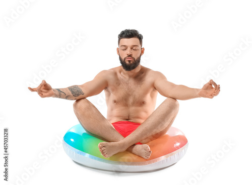Meditating young man with inflatable ring on white background