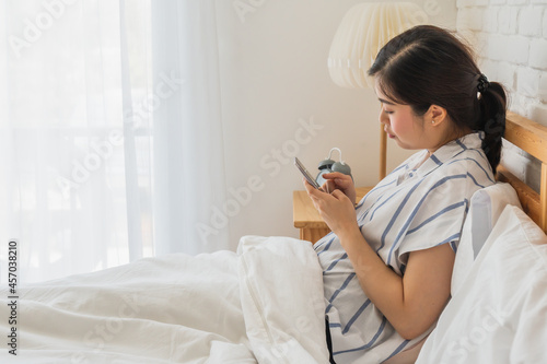 asian woman lying on bed using smartphone for chatting