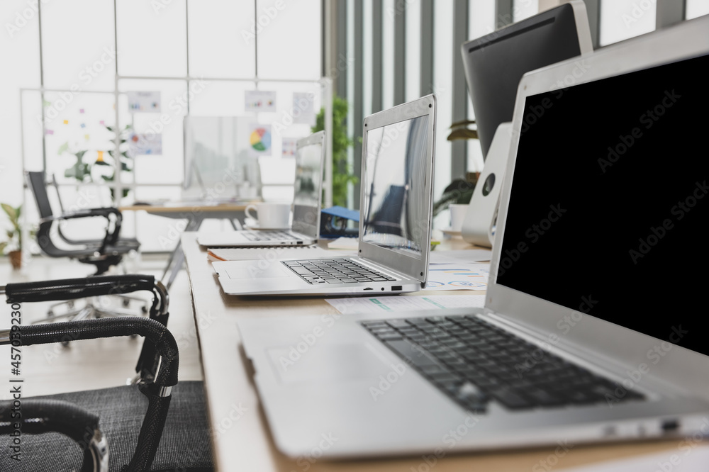 Selective focus on laptops sitting on conference table in meeting room office with multiple glass windows in background Selective focus on laptops sitting on conference table in meeting room office with multiple glass windows in background