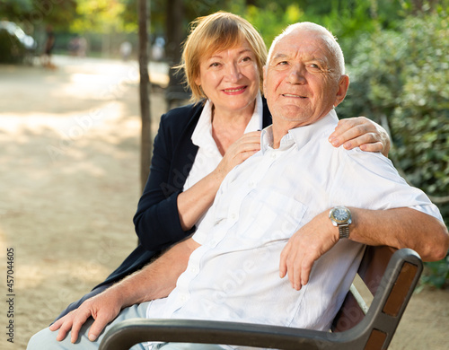 Portrait of senior couple in love sitting on bench in park on sunny day © JackF