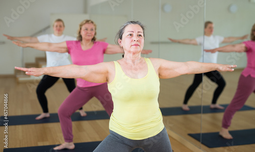 Elderly women practicing yoga - virabhadrasana pose photo