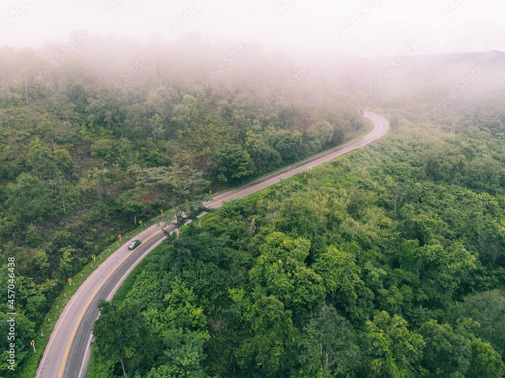 Aerial view foggy road forest tree environment nature background, mist on green forest top view foggy landscape the hill from above, wood tree road curve to mountain background