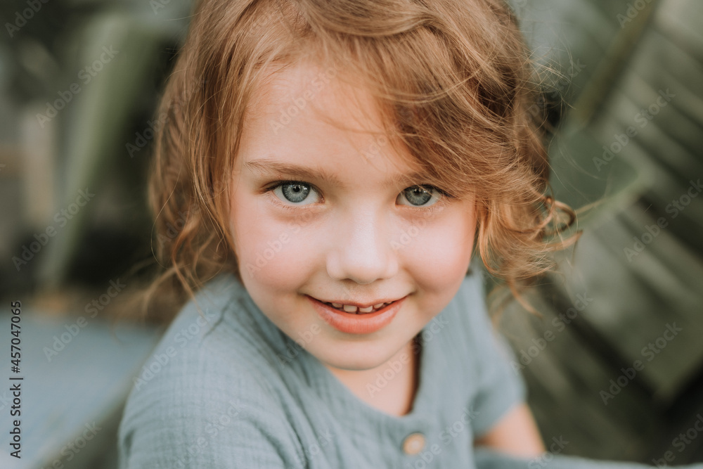 The face of a little girl surrounded by tropical leaves. A closeup portrait of a beautiful baby with perfect skin and blonde hair. Natural cosmetics, health, cleanliness, skin care, beauty concept The face of a little girl surrounded by tropical leaves. A closeup portrait of a beautiful baby with perfect skin and blonde hair. Natural cosmetics, health, cleanliness, skin care, beauty concept