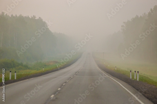 smooth asphalt road fades into fog on a warm summer morning