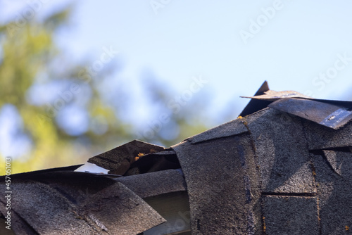 old damaged shingles piled up draped over edge of roof