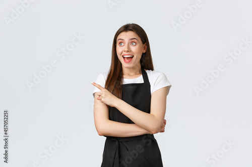 Small business, employees and coffee shop concept. Excited happy and smiling cafe worker looking astonished and pointing left. Impressed cute store employee react to cool advertisement