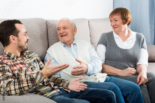 Elderly grandparents friendly conversation with grandson sitting on sofa