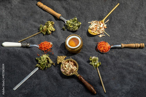 Various teas and dried herbs assortment on spoons in rustic style with honey on balck background.