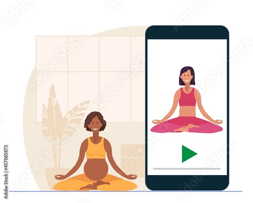 Online yoga. Pregnant African American woman sitting in lotus position on mat at home. Woman watches at yoga lessons on your phone. Prenatal yoga, meditation, relax, recreation, healthy lifestyle.
