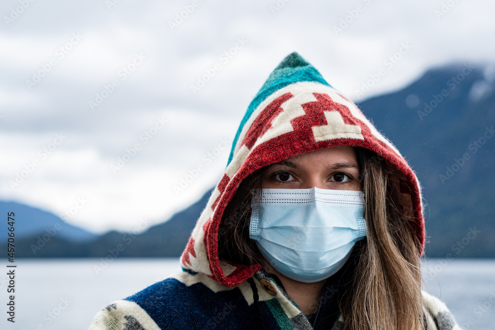 Portrait of a young blonde woman with a defiant look wearing a colorful poncho and a covid medical mask 19