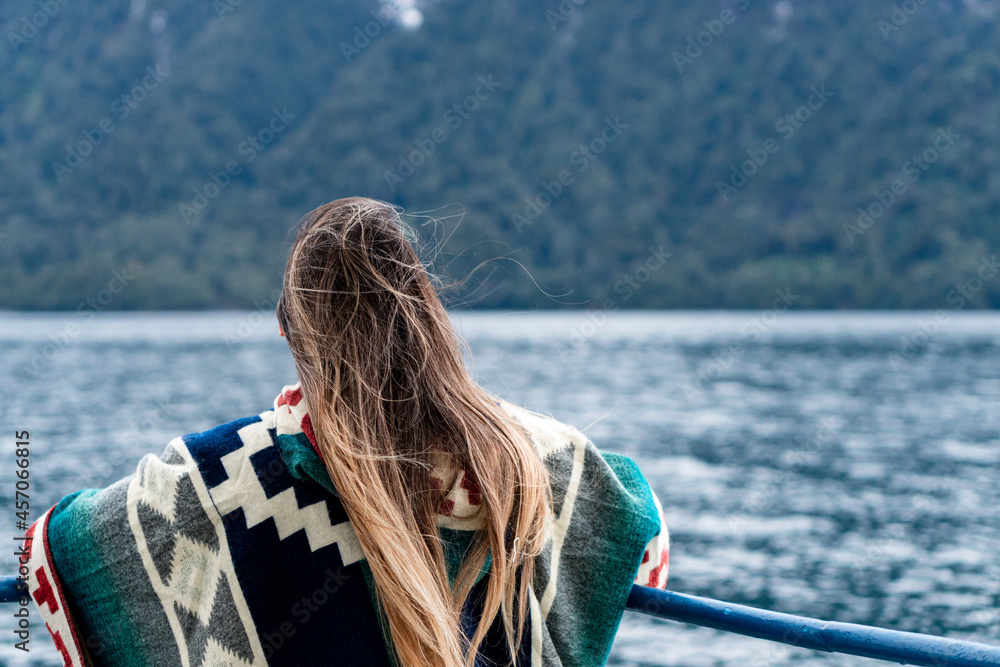 Fototapeta premium Young woman wearing a colorful poncho looking towards the snow-capped mountains on the way to peulla