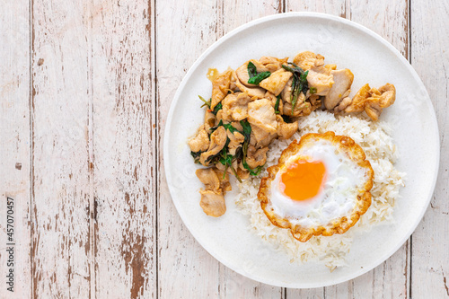 Khao Pad Ka Prao Gai Kai Dao, Thai food, streamed rice topped with basil stir fried chicken and fried egg in white ceramic plate on white old wood texture background with copy space, top view