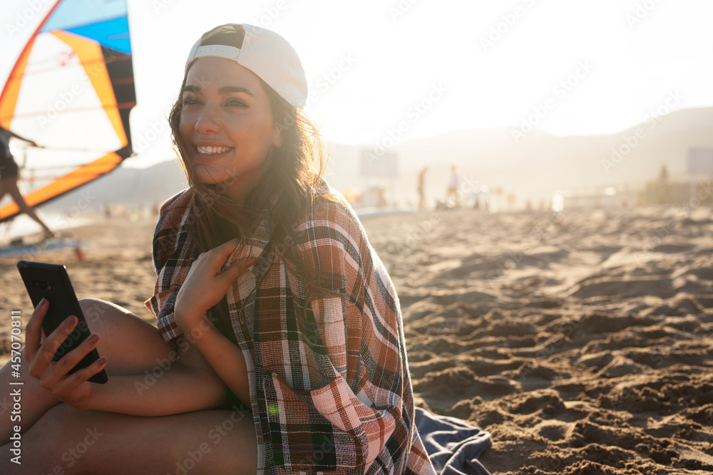 Portrait of beautiful female surfer with her surfboard. Young woman having video call while relaxing at the beach.