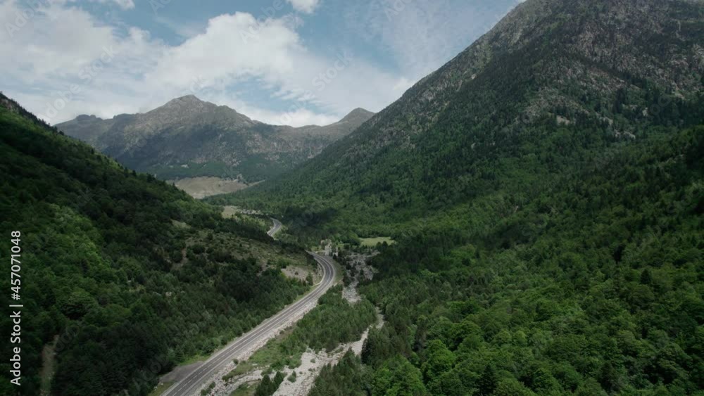 Beautiful drone view of an asphalt road in high mountains. The mountain range disappears in the sky, slightly cloudy skies but the peaks are lit by the sun. Beautiful drone view of an asphalt road in high mountains. The mountain range disappears in the sky, slightly cloudy skies but the peaks are lit by the sun.