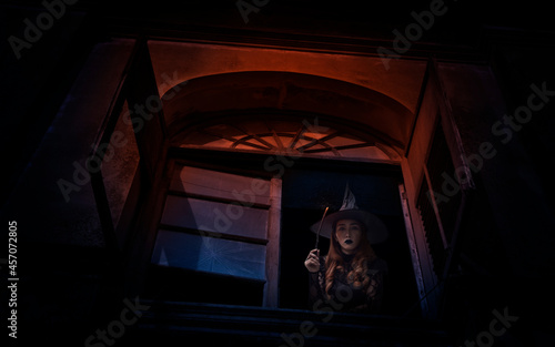 Halloween witch holding magic wand standing in old ancient window castle, Halloween mystery concept