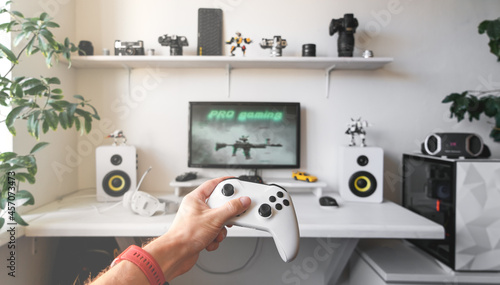 Close-up of male hands holding white wireless gamepad against white computer dream desk. photo