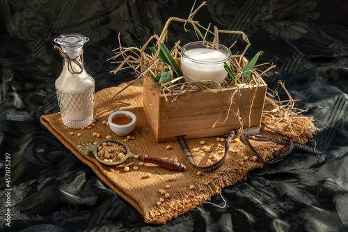 Soy products : A glass of Homemade soy milk and grains (soybeans) in wooden box Served with brown sugar and honey with lighting in the morning. Alternative milk concept, Copy space, Selective focus.