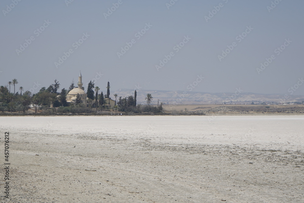 Fototapeta premium Larnaca, Cyprus, September 2021: Hala Sultan Tekke Mosque on the background of a salt lake. Dried up salt lake. Natural salt on the surface of the earth