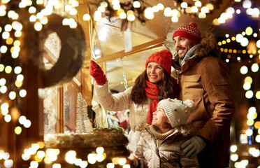 family, winter holidays and celebration concept - happy mother, father and little daughter at christmas market on town hall square in tallinn, estonia