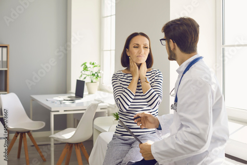 Lady with inflamed tonsil glands visits doctor at clinic. Worried woman asks specialist to help reduce neck pain. Man who works as general practitioner talking to female patient with sore lymph nodes photo