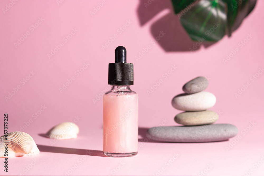 Cosmetic product in a glass bottle with a pipette on a pink background. Smooth stones nearby. The concept of skin care, cosmetology.