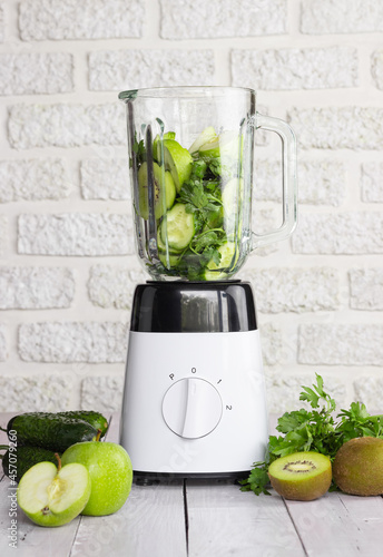 Blender with green fruits and vegetables on a light background. Preparation of a healthy smoothie.