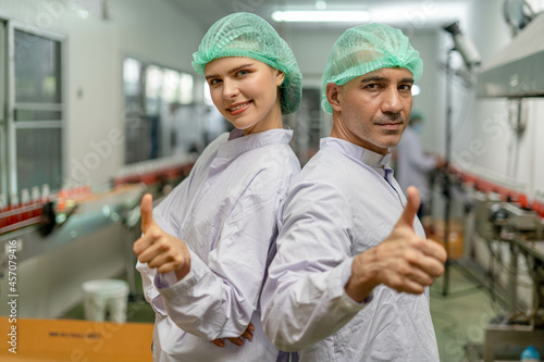 A quality supervisor or a food technician is inside the juice chamber. Employees are happy to work within an industrial facility. Male and female officers dressed in white and wearing hats
